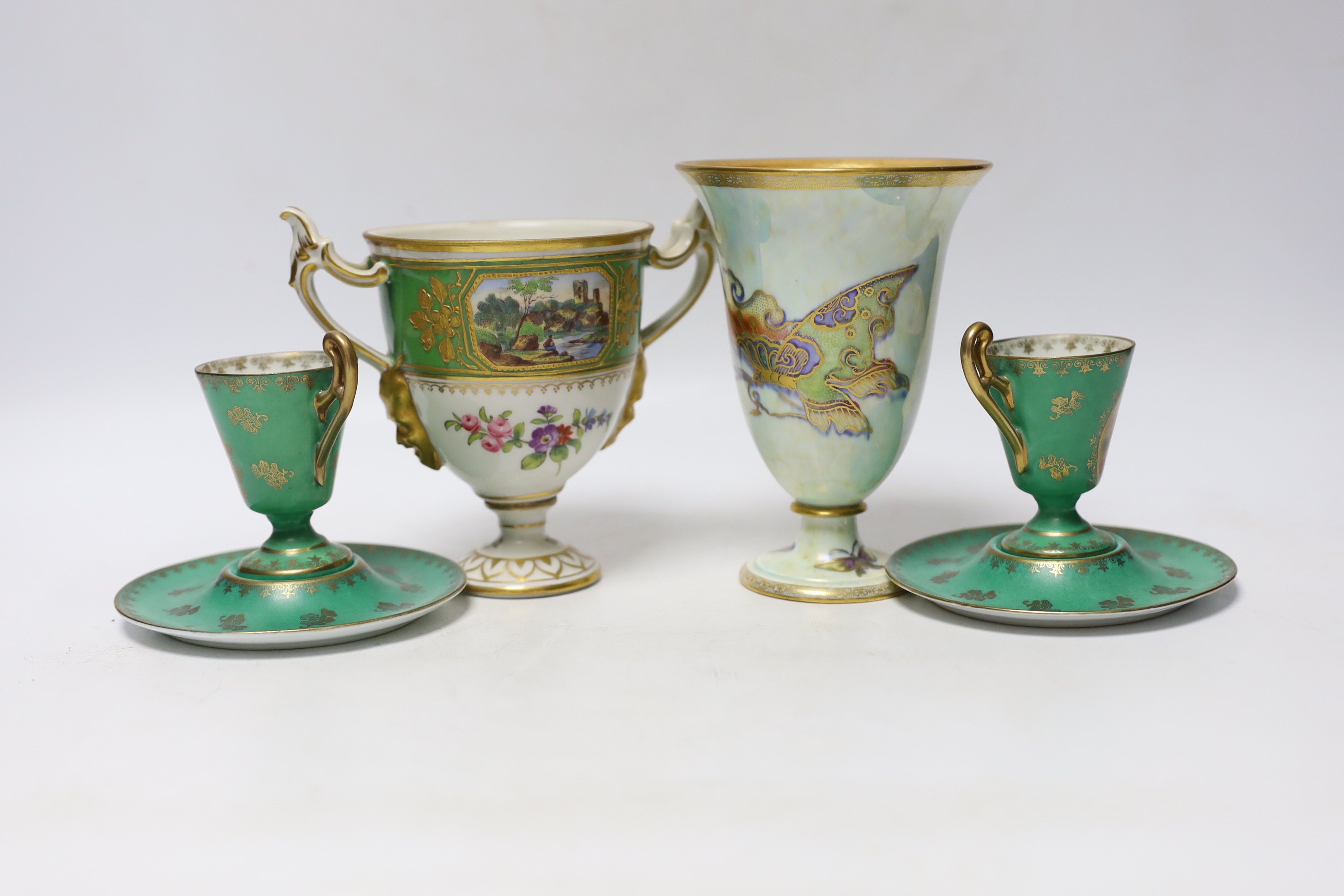 A Continental porcelain twin handled trophy cup with landscape vignettes, together with a pair of Continental liqueur cups and dishes, and a Wedgwood butterfly lustre posy vase, design number Z4832, vase 13.5cm high (4)